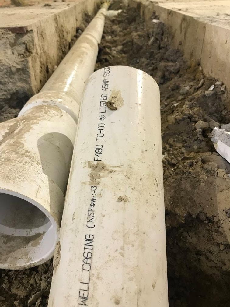 Large white PVC pipes laid in a muddy trench at a construction site