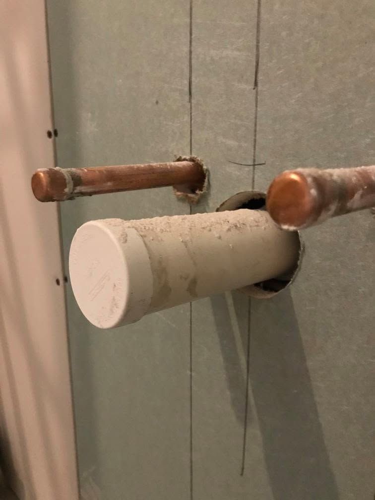 White toilet paper roll on a wall-mounted holder beside two copper pipes.