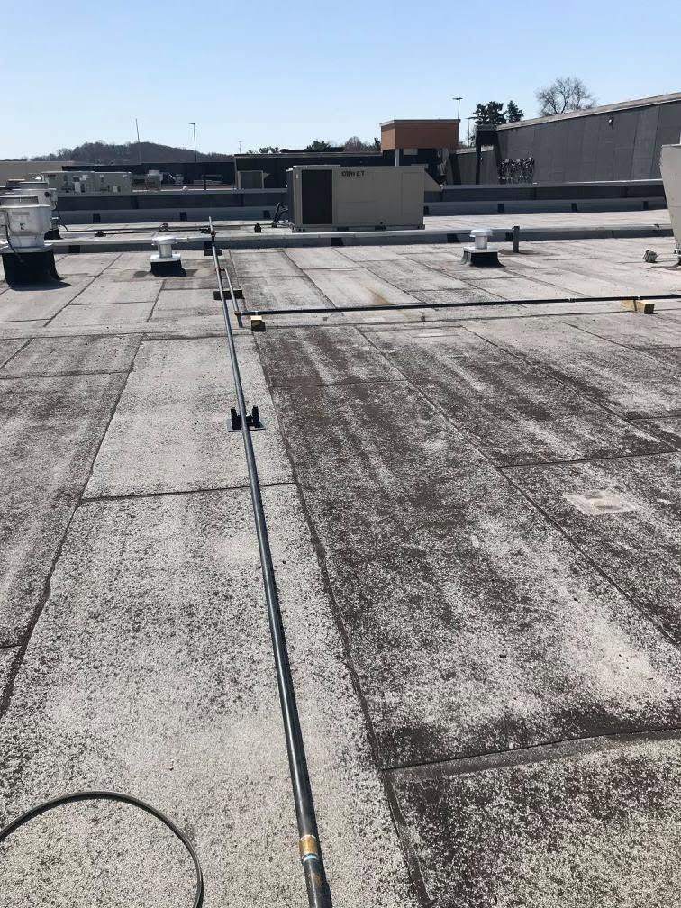 Flat commercial rooftop with HVAC units, vents, and weathered membrane under a clear sky.