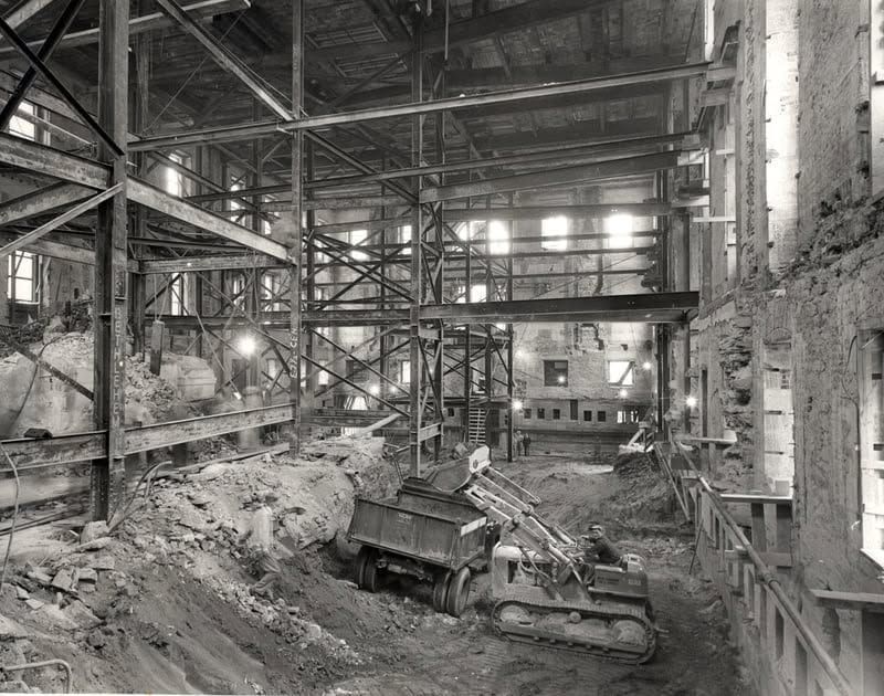 Abandoned industrial factory interior with rusted machinery, debris, and steel beams under broken skylights