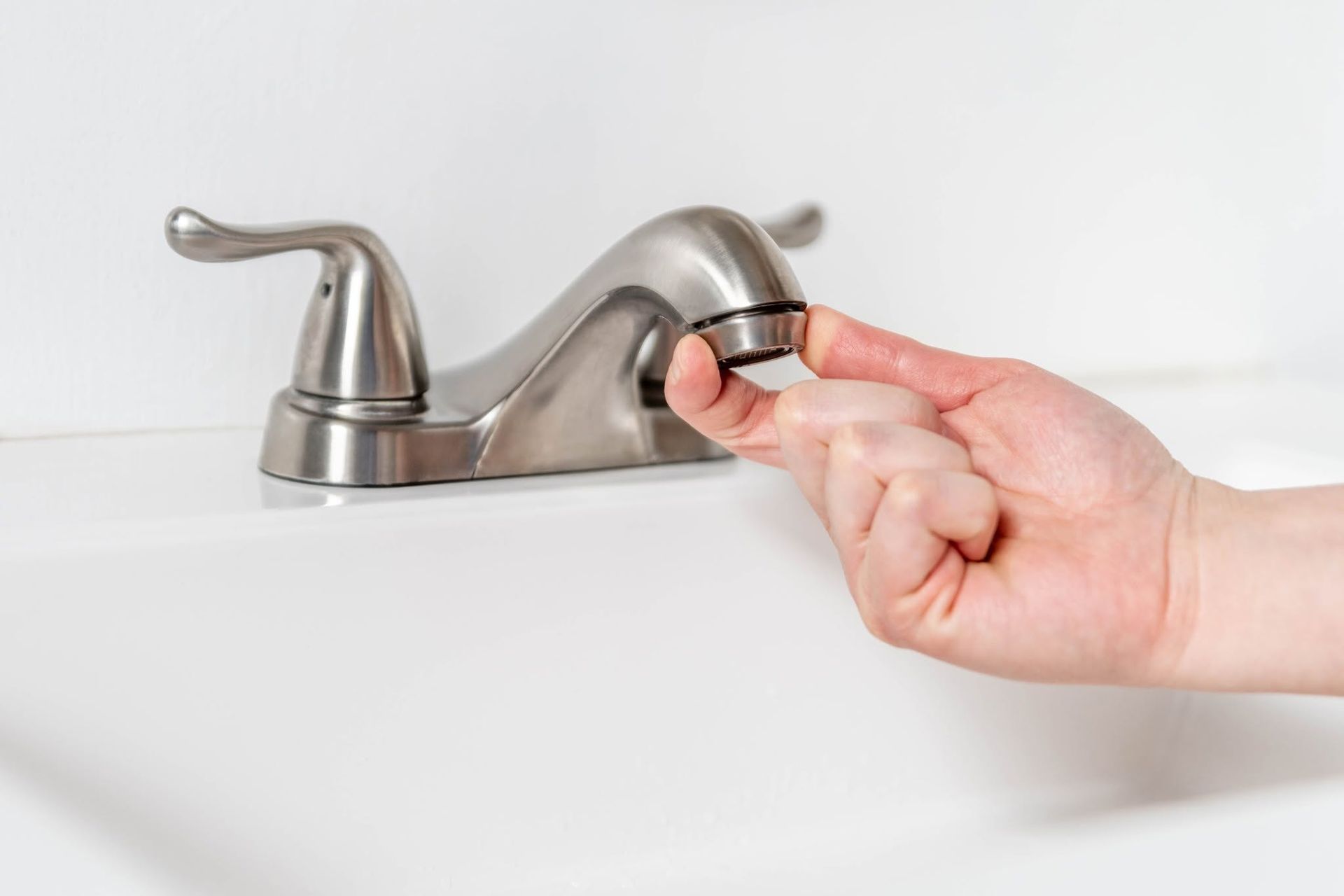 Hand turning a faucet knob on a bathroom sink