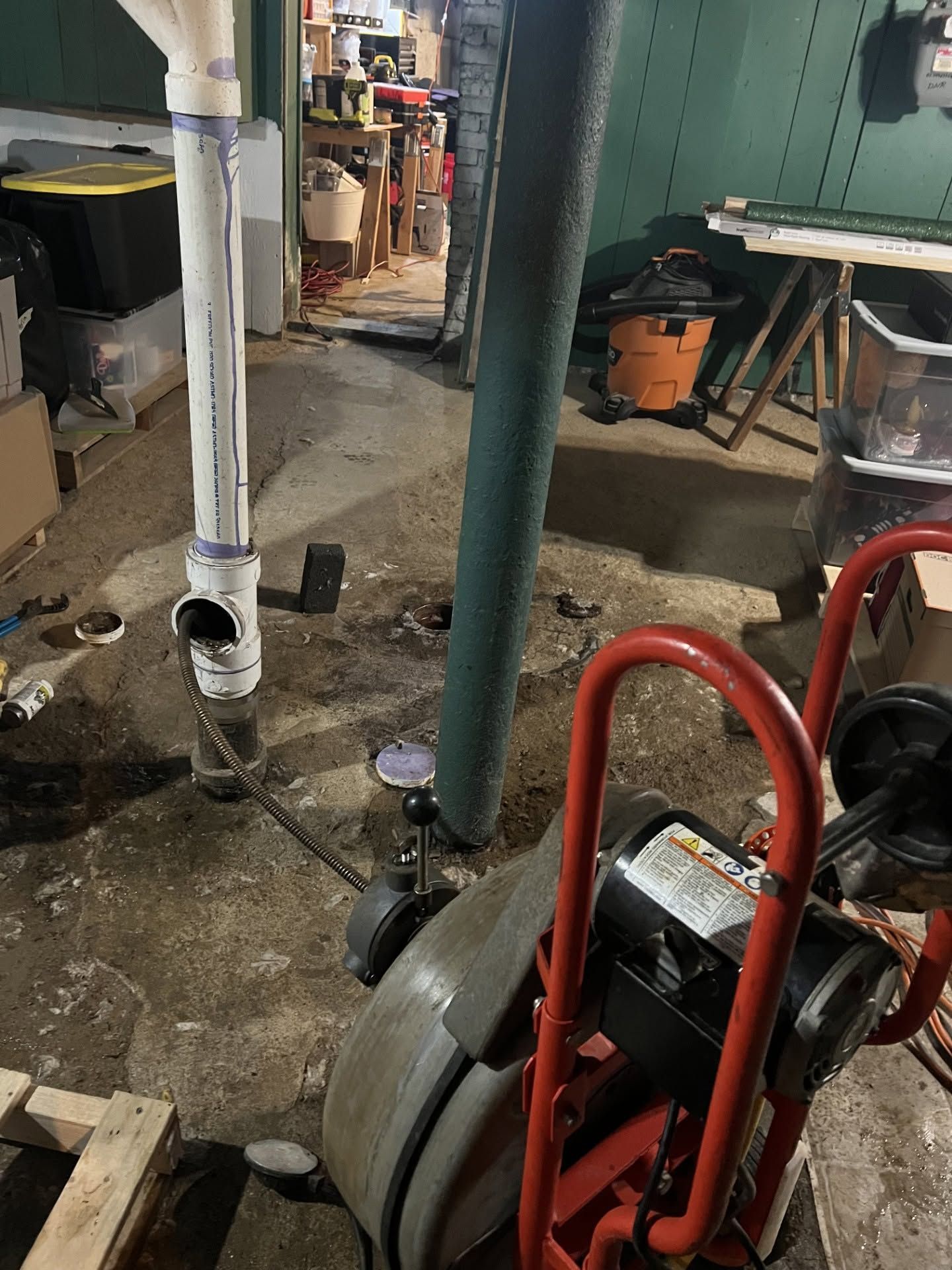 Basement utility area with a drain snake machine, white pipe, and workbench in the background