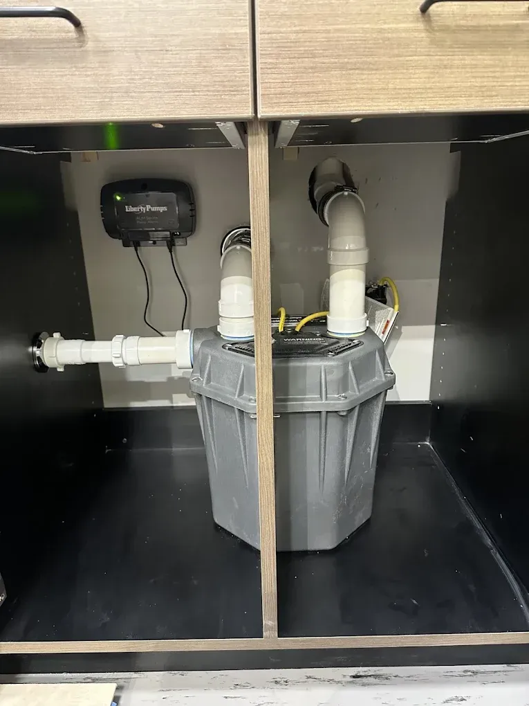 Under-sink plumbing with a gray bucket catching drainage in a cabinet.