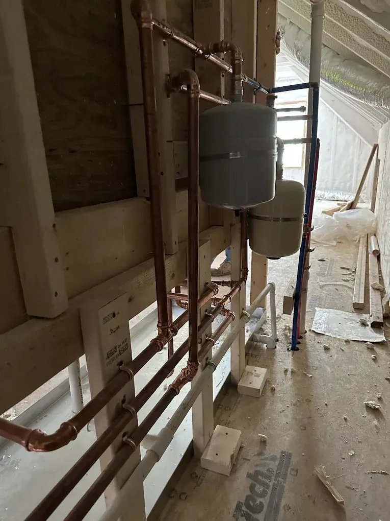 Copper pipes and two water heaters in a narrow unfinished attic corridor