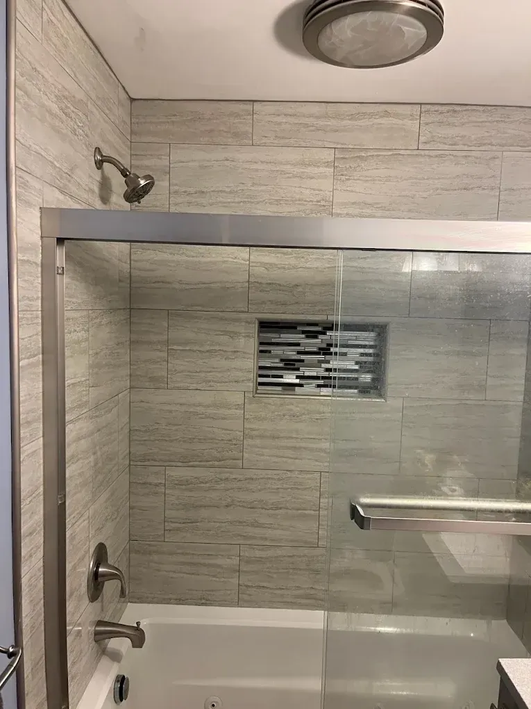 Small tiled bathroom with a bathtub, glass shower door, chrome fixtures, and ceiling light.