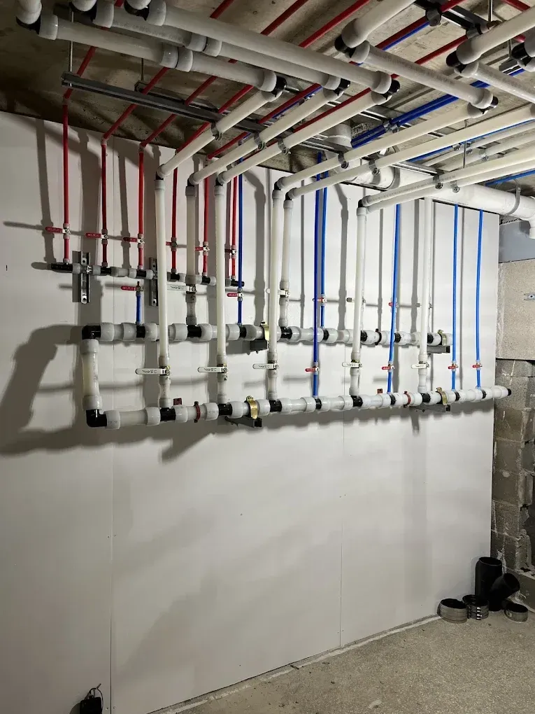 Residential utility room with exposed pipes, valves, and a wall-mounted manifold system