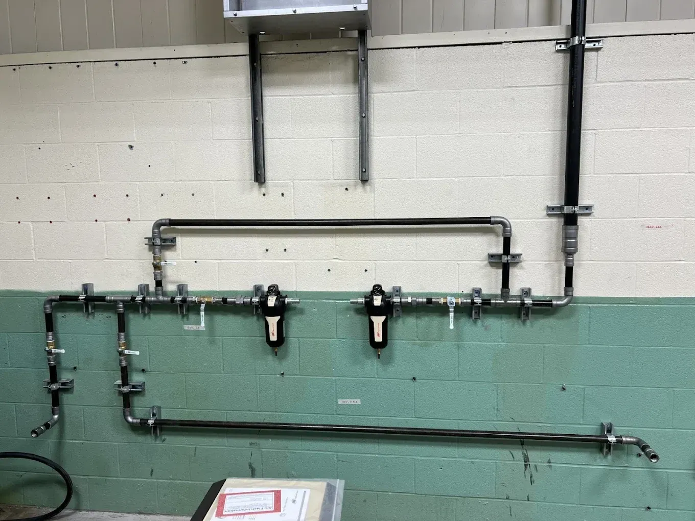 Industrial wall with exposed metal piping and valves above a green-painted lower section