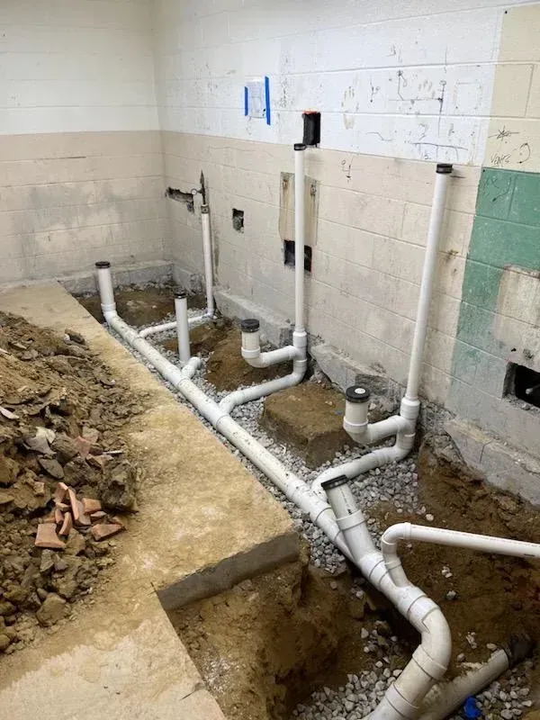 Plumbing trench with exposed white pipes and rubble in a tiled room under renovation