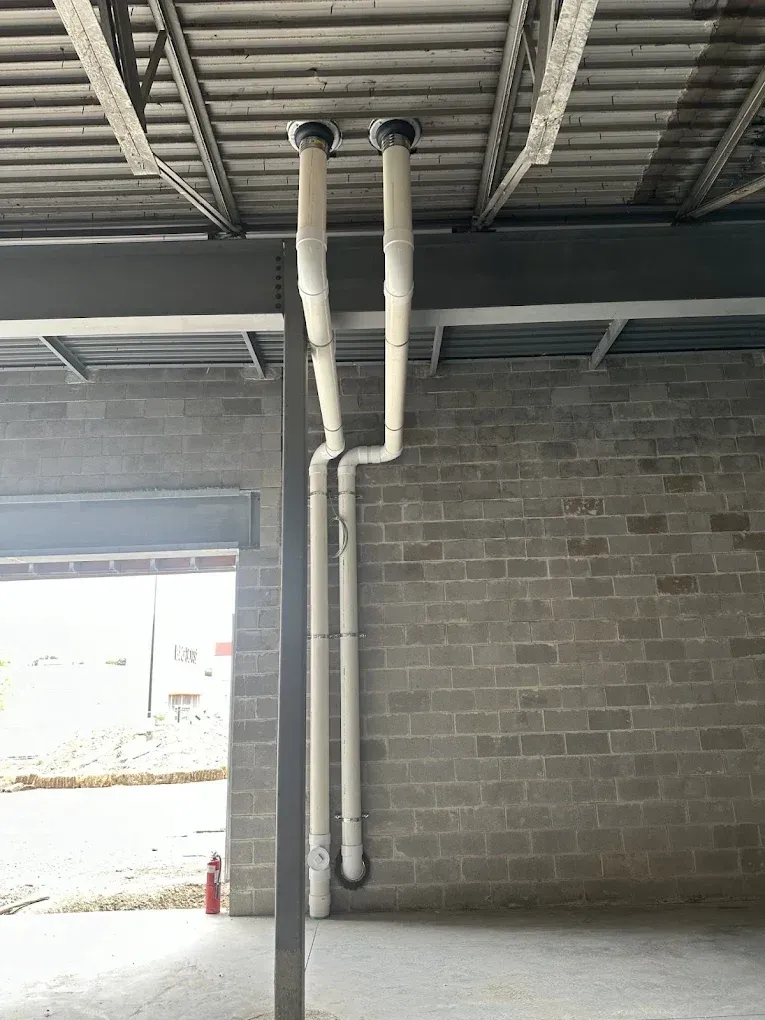 Interior cinderblock wall with exposed white pipes and an open doorway to the outside