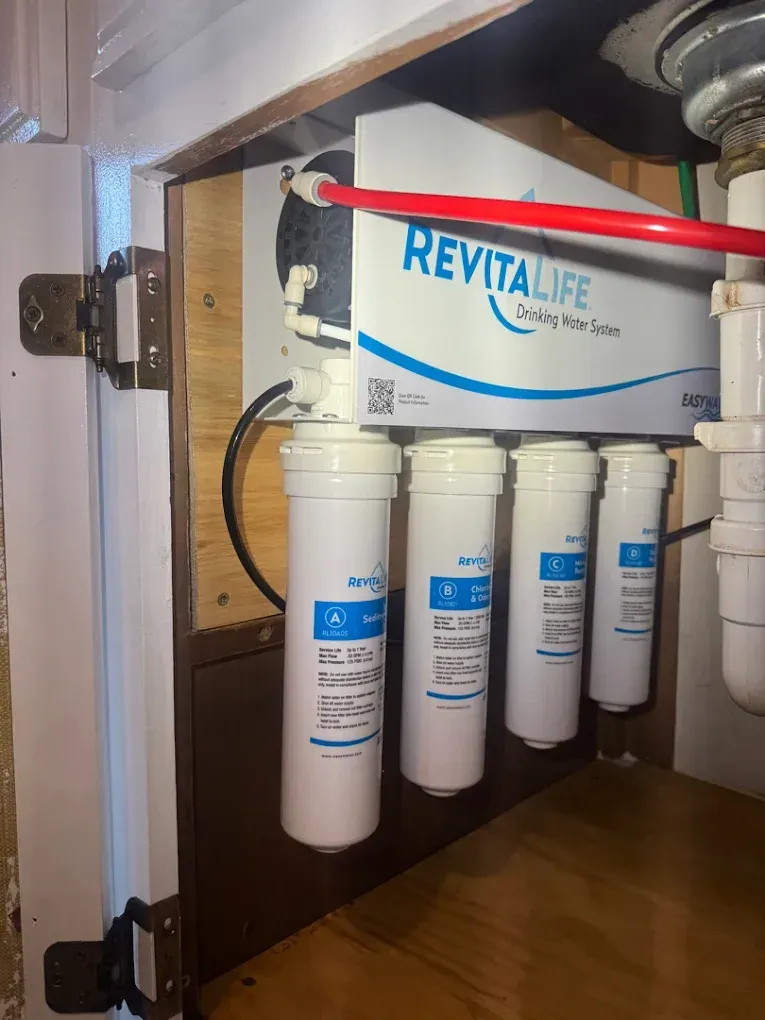 Wall-mounted under-sink water filtration system with four white canisters and a blue RevitaLife label