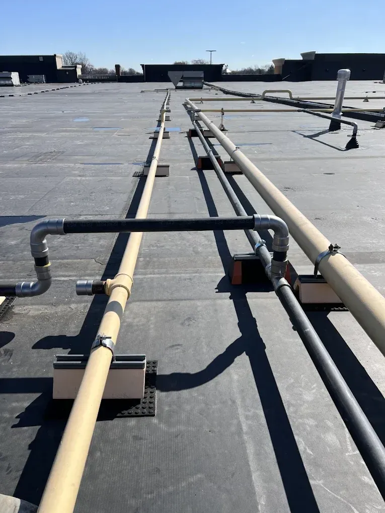 Rooftop with parallel beige pipes and dark metal rails crossing a flat gray surface under a clear sky
