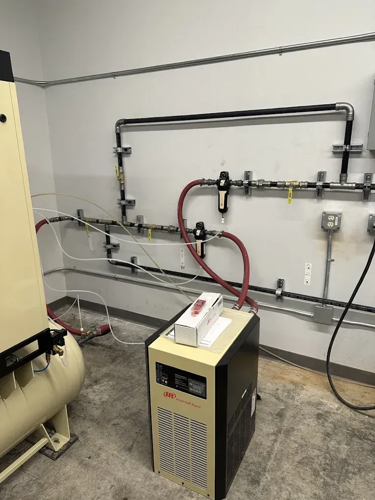 Industrial room with a beige machine connected to red hoses and wall-mounted piping.