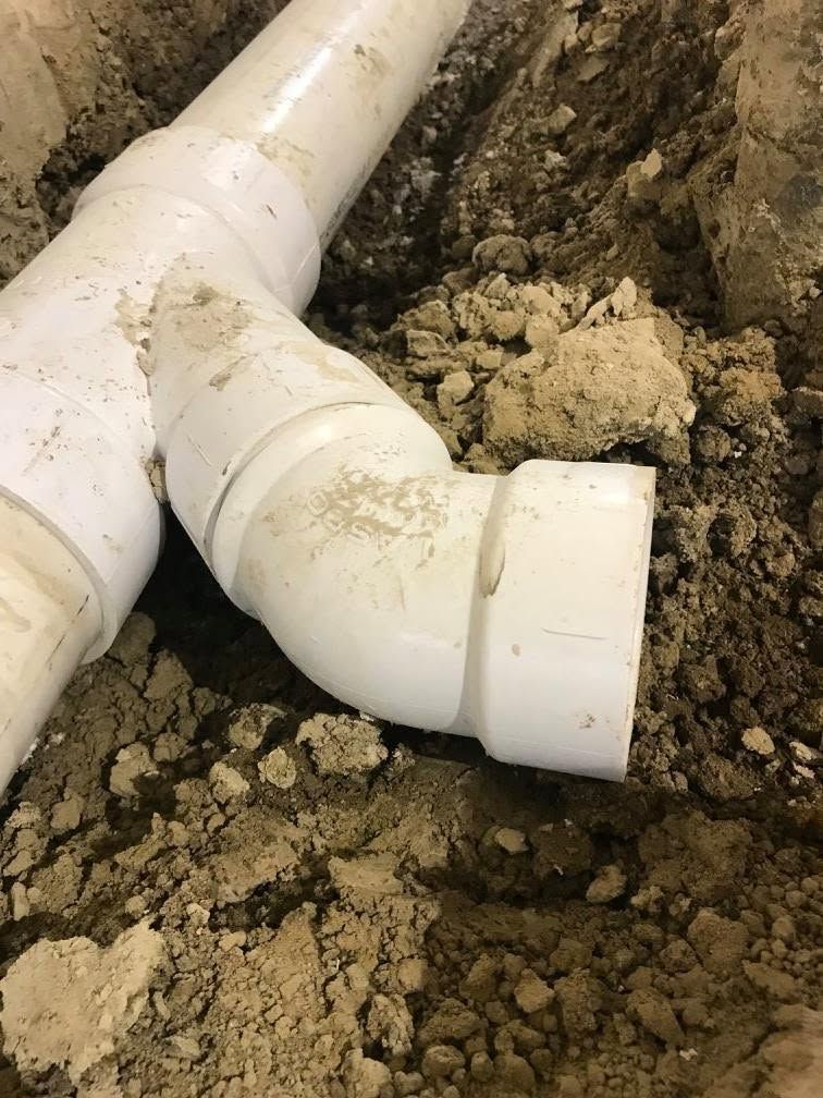 White PVC pipe elbow joint in a dirt trench during underground plumbing work