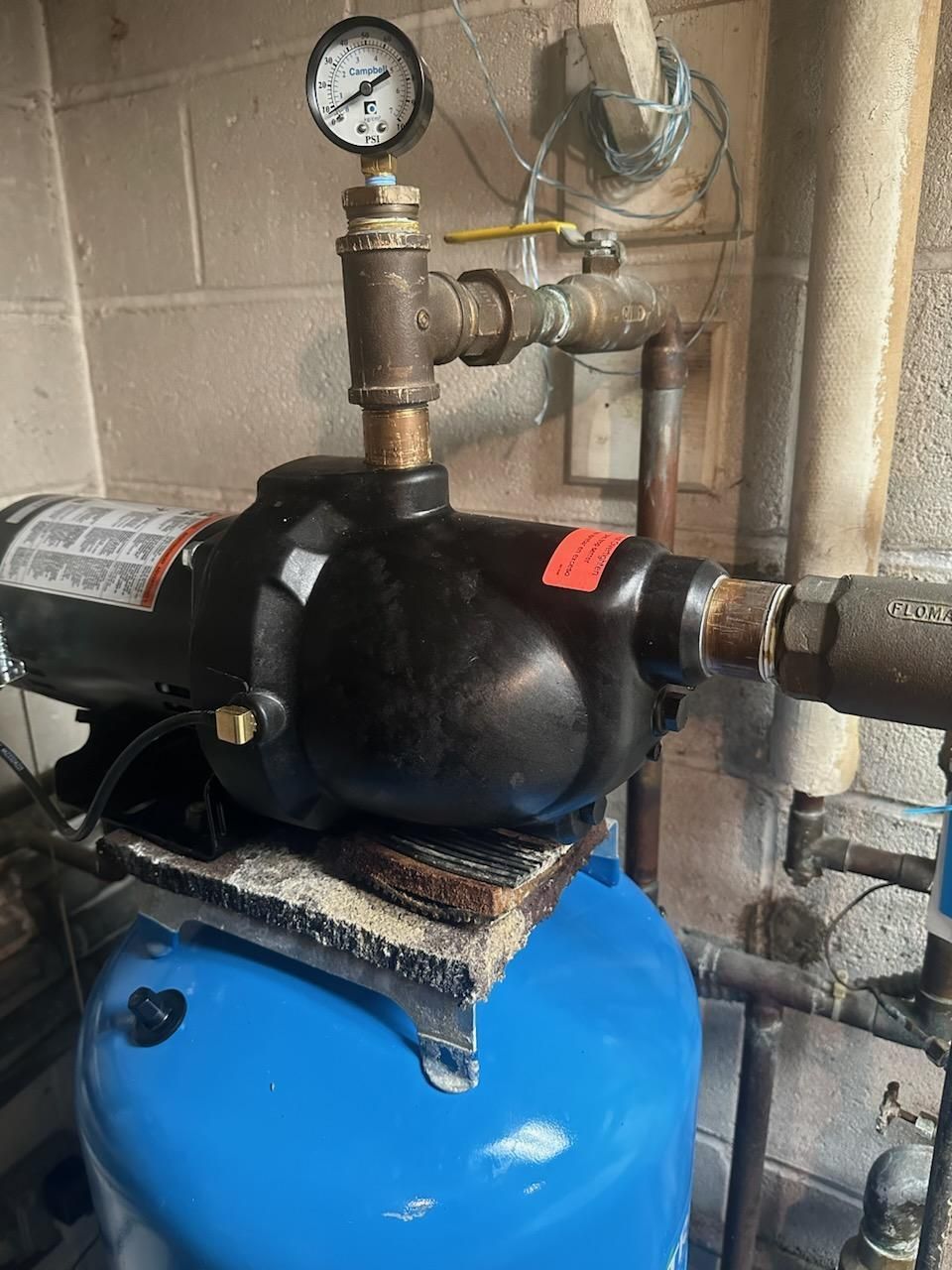 Industrial pressure tank with gauge and black valve assembly on a blue base, in a utility room