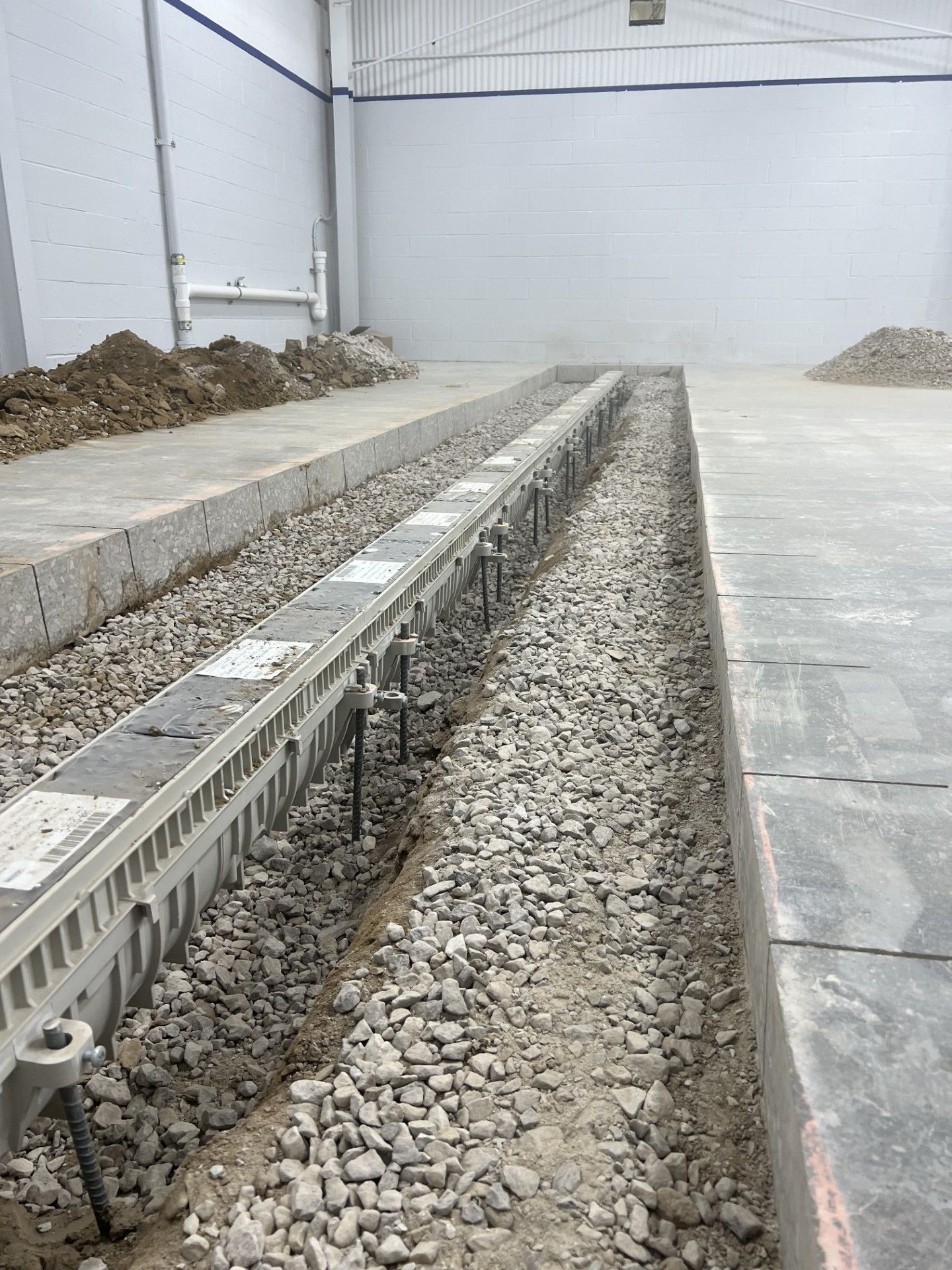 Construction site trench with gravel and concrete channels beside a paved floor