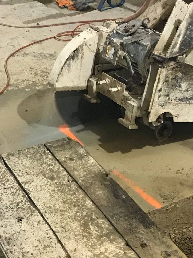 Concrete saw cutting a floor slab, spraying water and marking a straight cut line with orange paint.