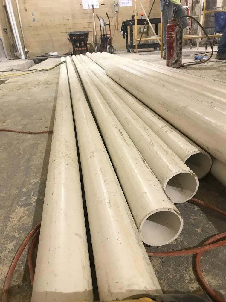 Long white PVC pipes laid on a workshop floor in an unfinished indoor space