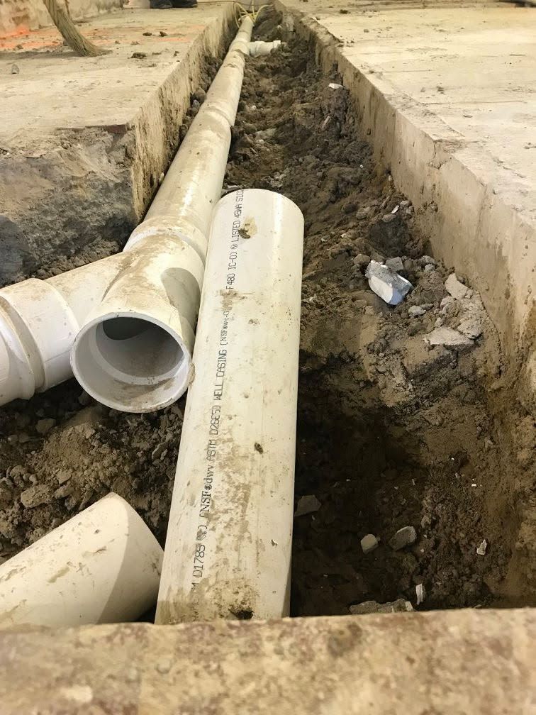 PVC pipes in a trench beside a concrete slab, with an open pipe joint visible.