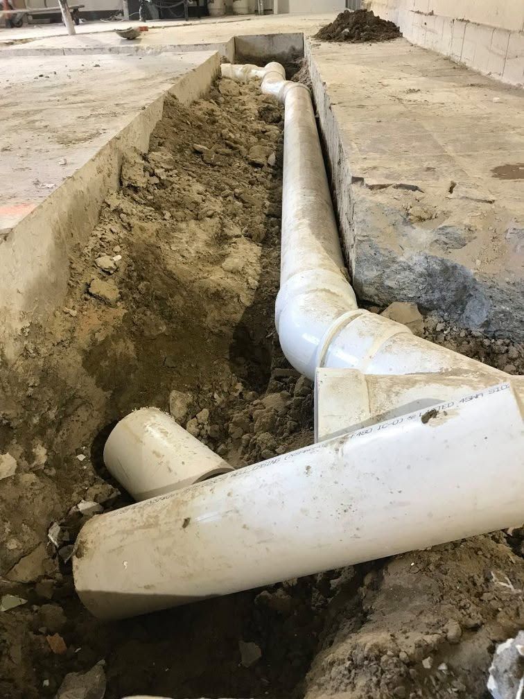 Broken white PVC pipes in a dirt trench at a construction site