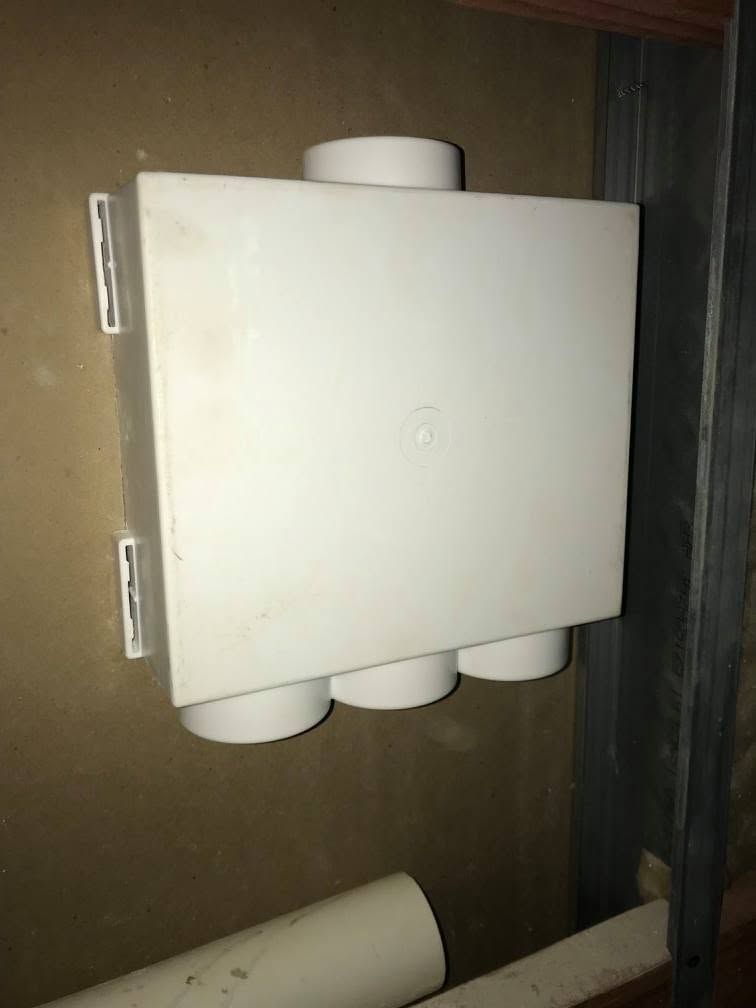 White wall-mounted device with several cylindrical outlets on a dark wall