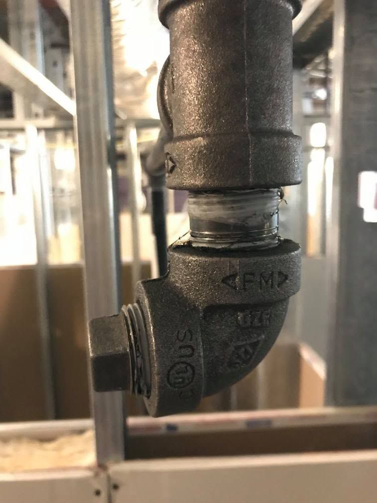 Close-up of a black metal pipe elbow joint with threaded fittings in an industrial setting