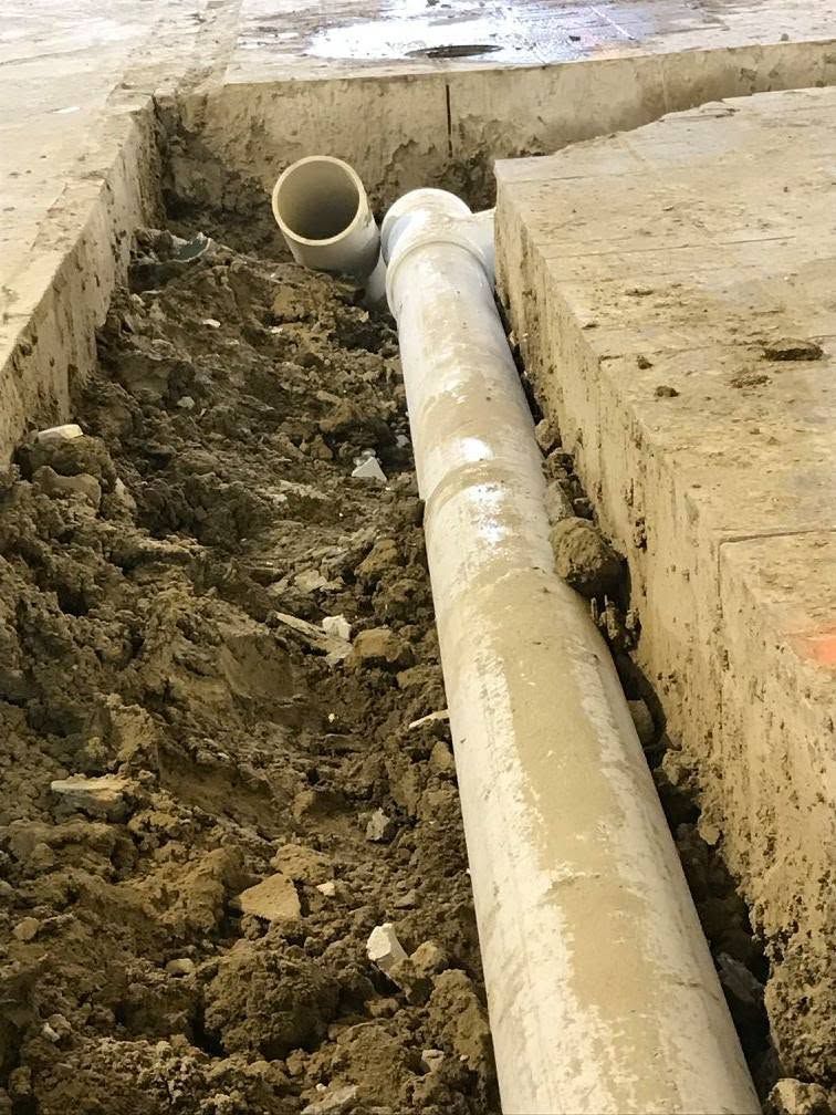 A dug trench with exposed beige sewer pipes and muddy soil at a construction site