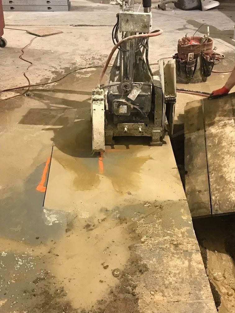 Small skid steer on a wet concrete worksite beside an open trench and orange cone