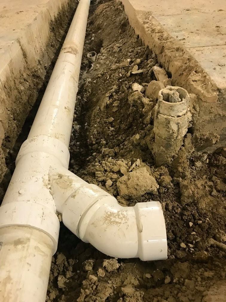 White PVC plumbing pipes in a dirt trench, with a T-joint and elbow fitting beside a capped pipe stub.