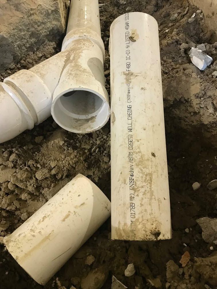 Broken white PVC pipes lying on dirt beside an exposed pipe joint
