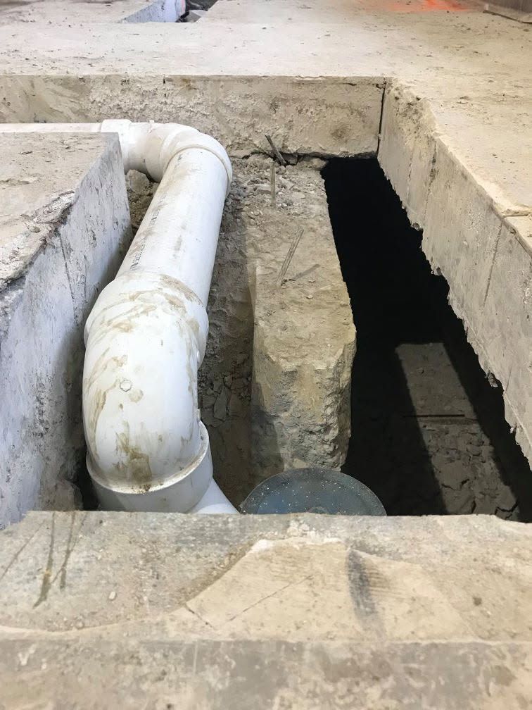 White PVC pipe over a concrete trench with an open dark shaft in an industrial area