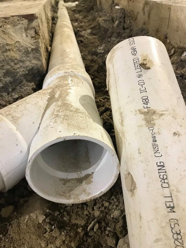 White PVC pipes laid in a dirt trench, with one large pipe opening facing the viewer.