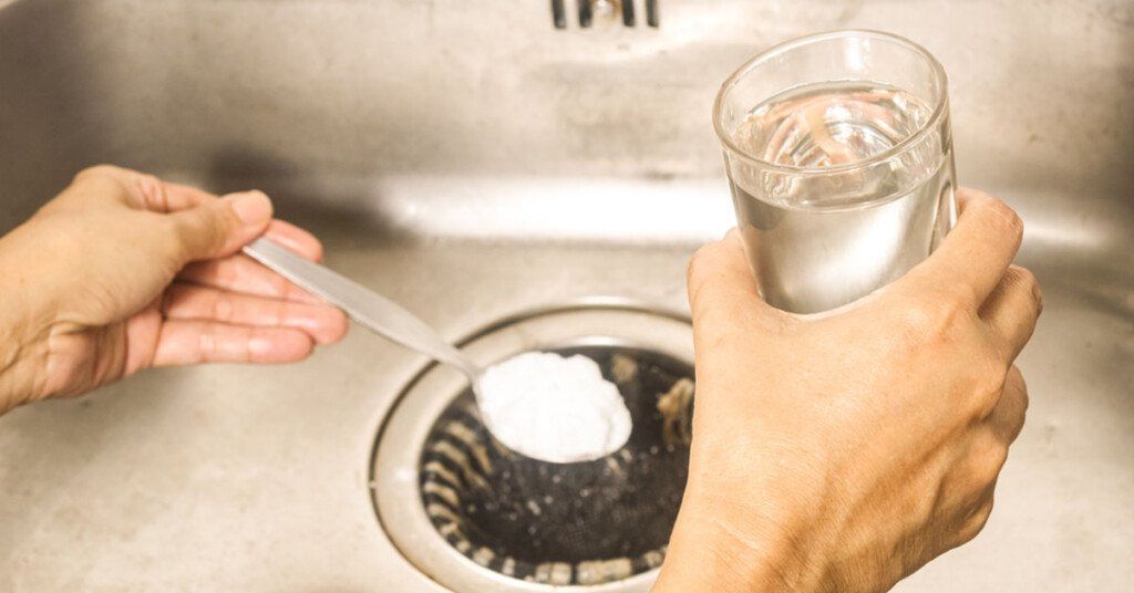 Hands pour baking soda and water into a kitchen sink drain to unclog it