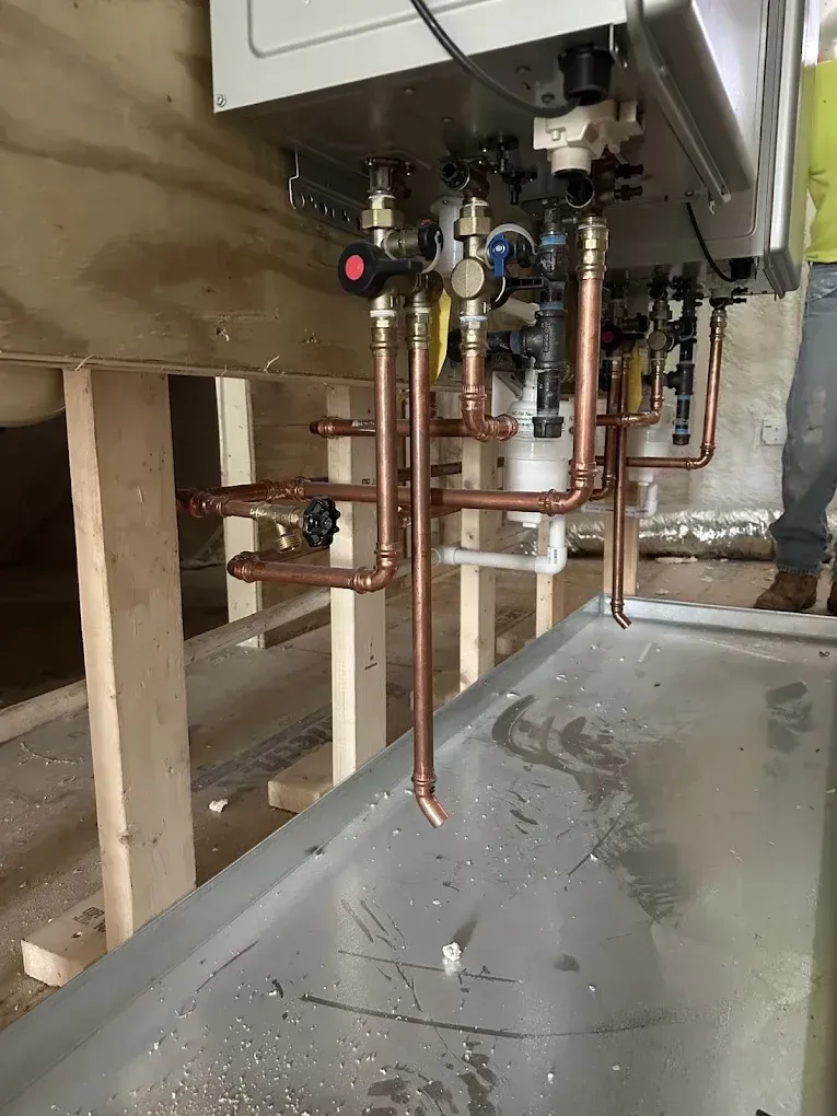 Under-sink plumbing with copper pipes, valves, and exposed framing in a utility space.