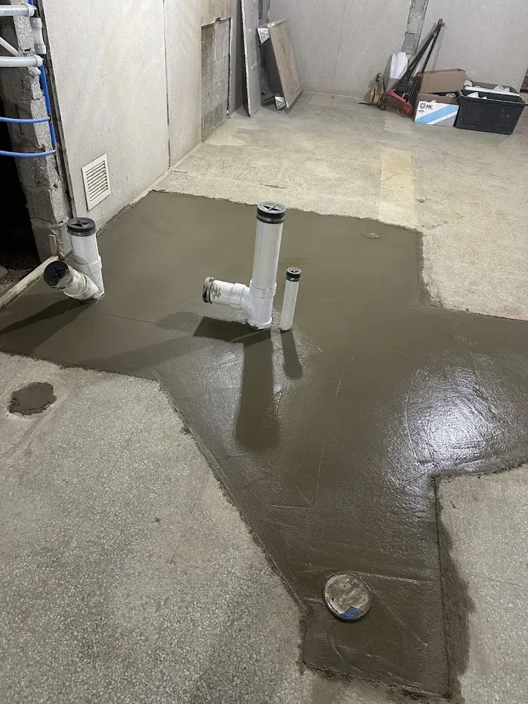 Wet concrete patch around a white pipe in an unfinished indoor room.