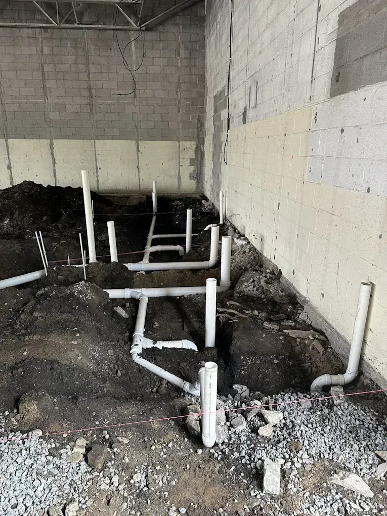 Construction site with white PVC pipes protruding from a gravel trench inside a concrete room.