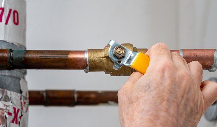 Hand using a yellow pipe wrench on a copper water pipe