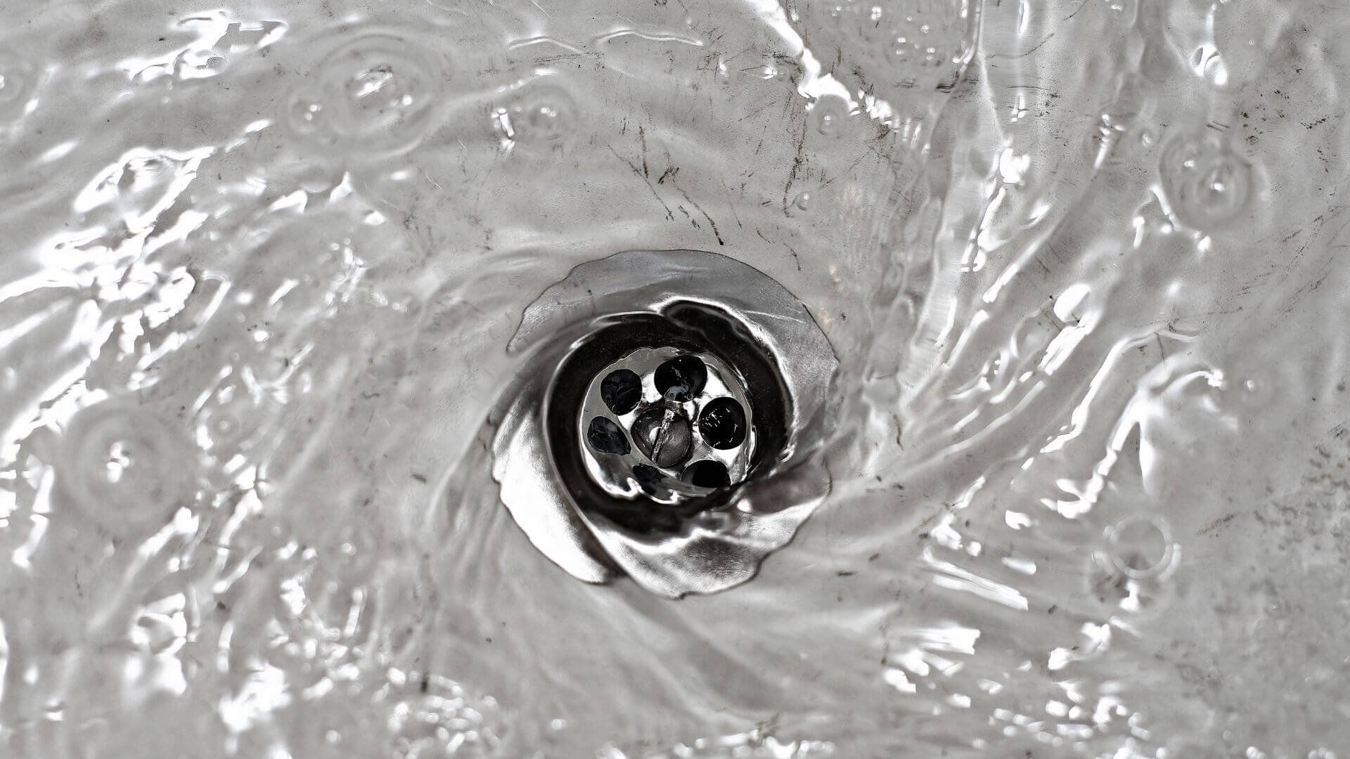 Close-up of a shiny metal sink drain with swirling water around it