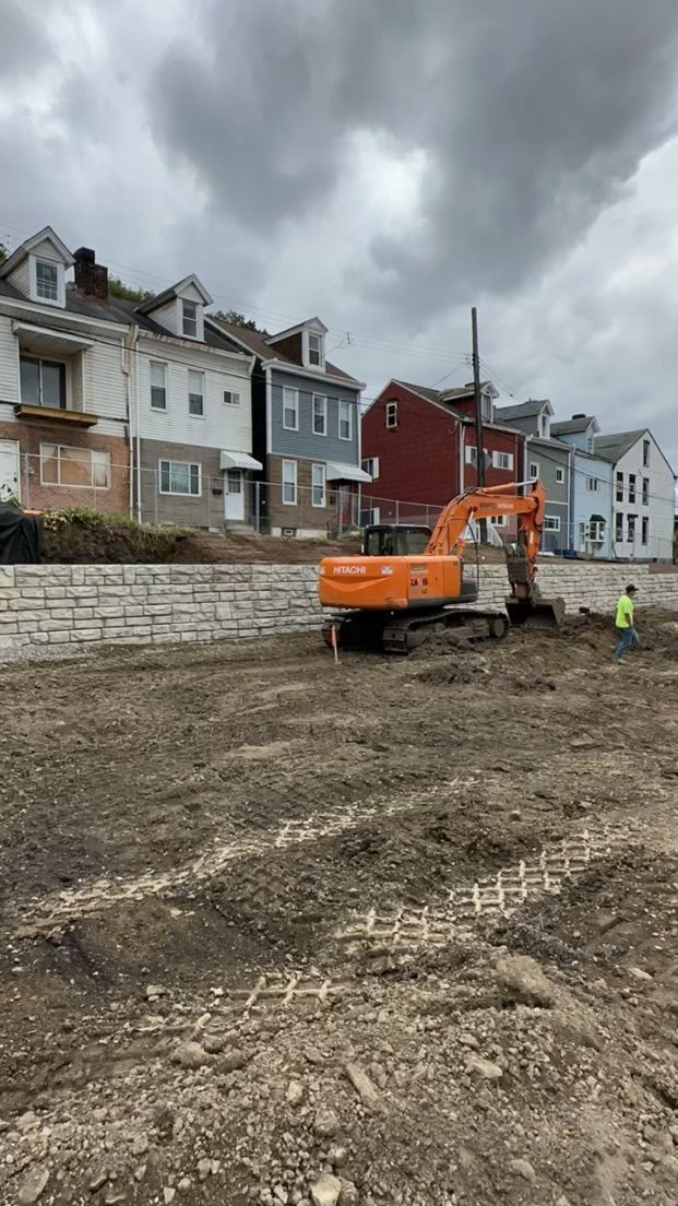 A large orange excavator is sitting in a dirt field in front of a row of houses.