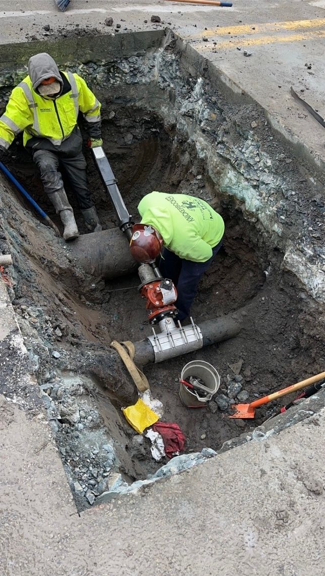 A man is working on a pipe in a hole in the ground.