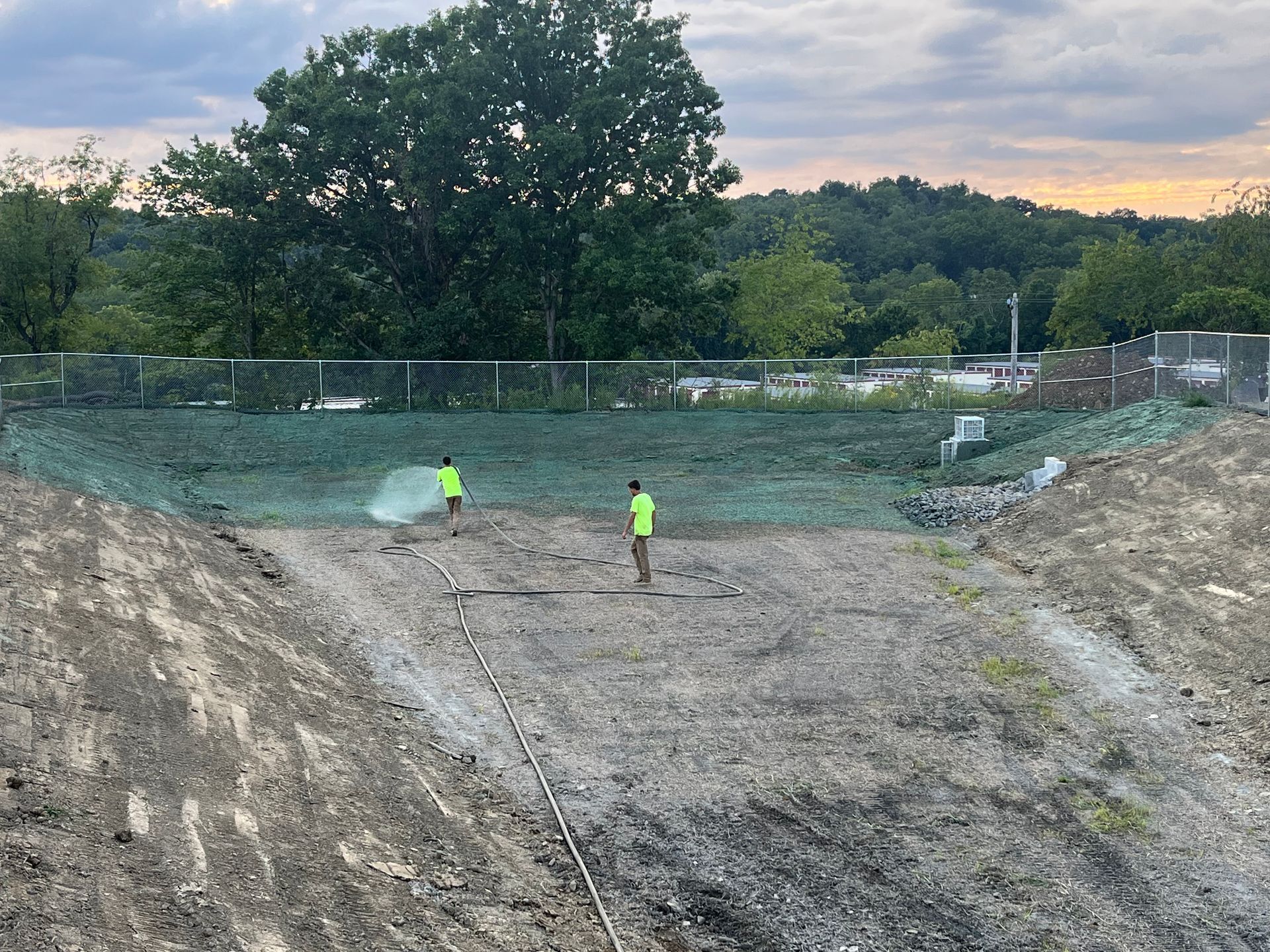 Two men are spraying water on a dirt field.