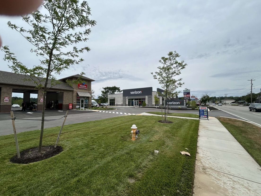 There is a fire hydrant in the middle of the grass in front of a car wash.