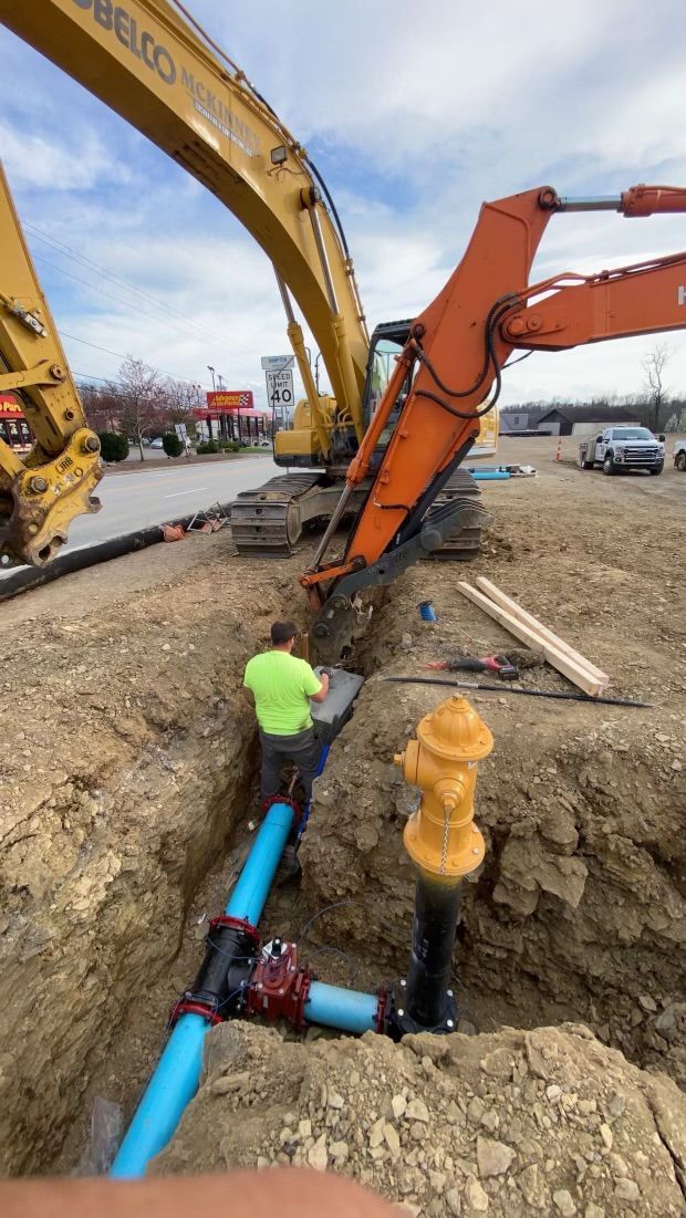A man is working on a pipe in the dirt next to a fire hydrant.