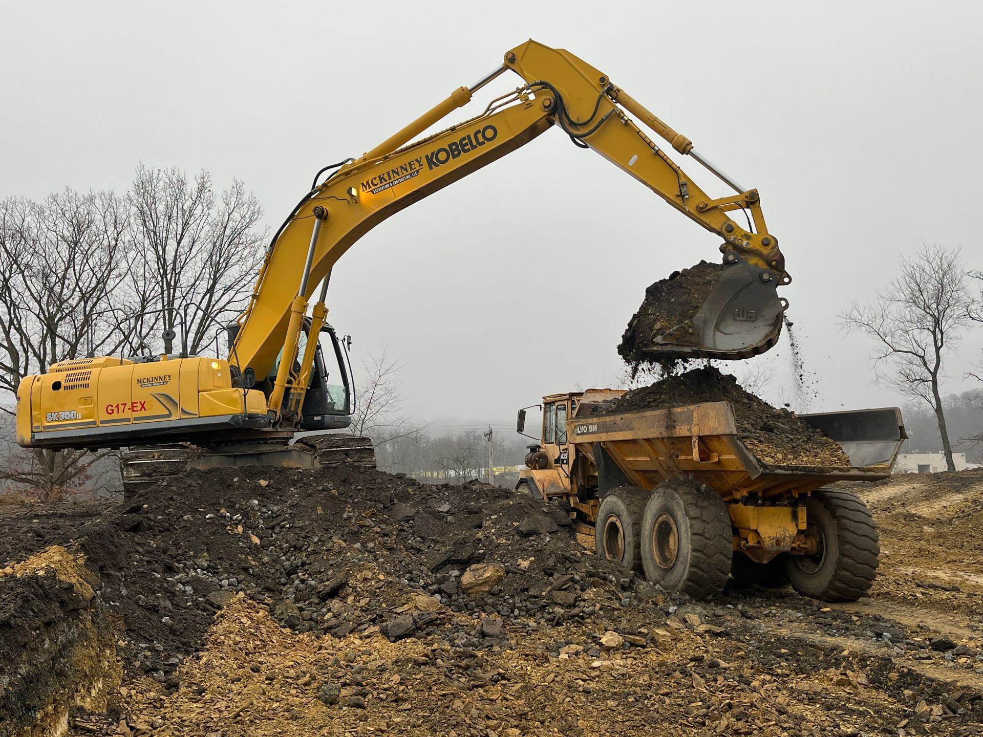 A yellow excavator is loading dirt into a dump truck.