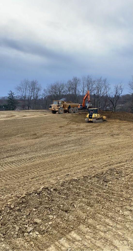 A group of construction vehicles are working on a dirt field.