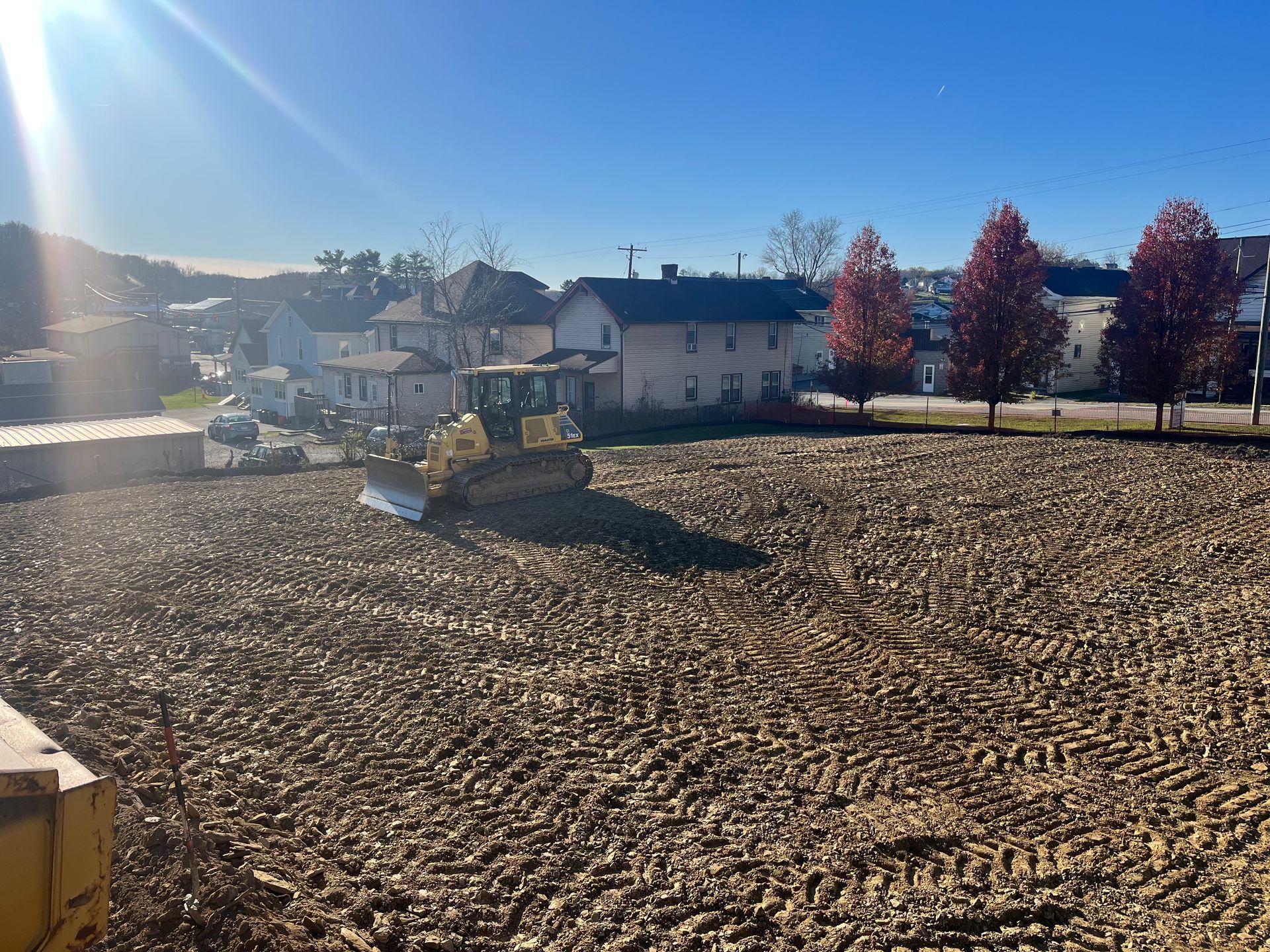 A bulldozer is moving dirt in a field with houses in the background