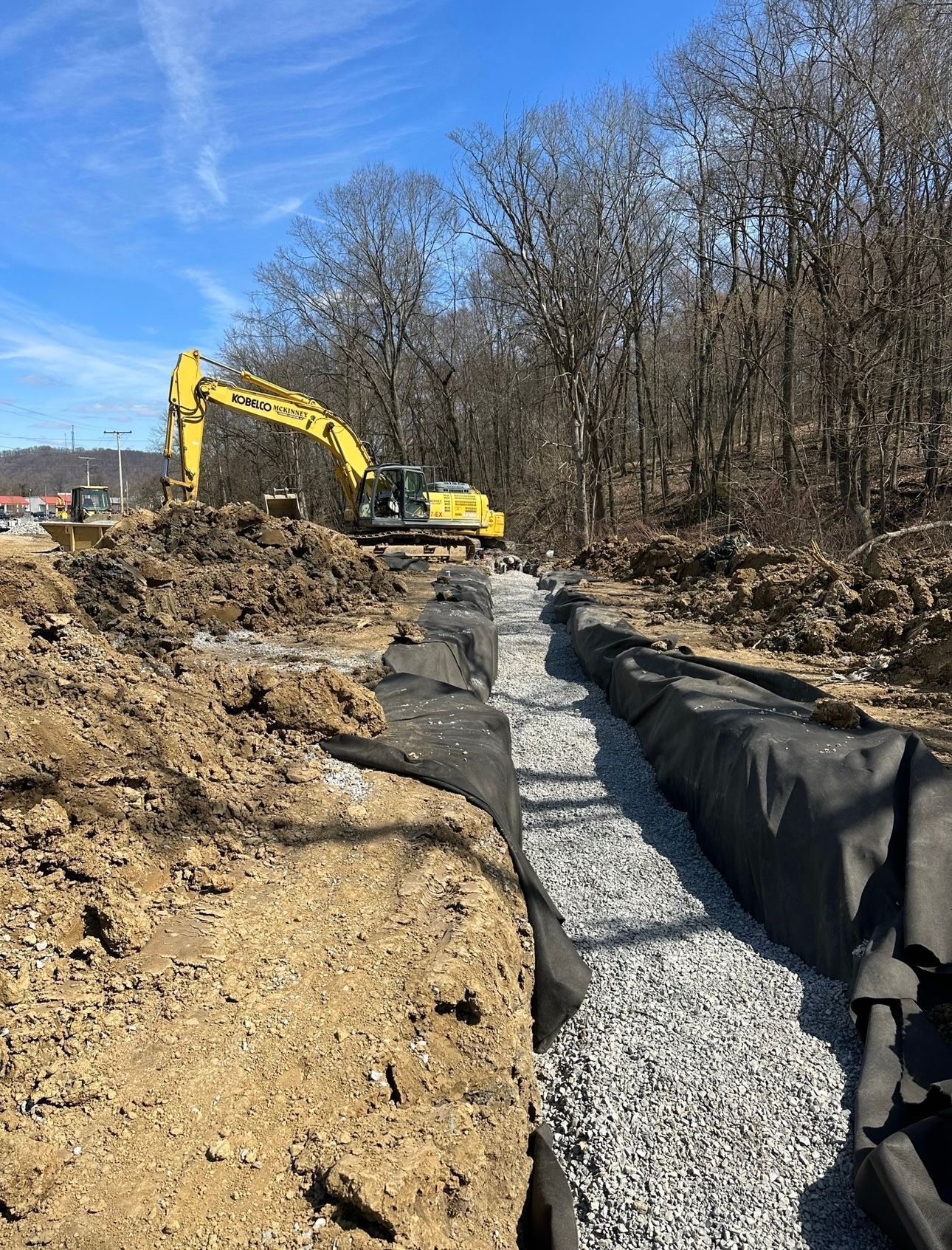 A yellow excavator is digging a trench in the dirt.