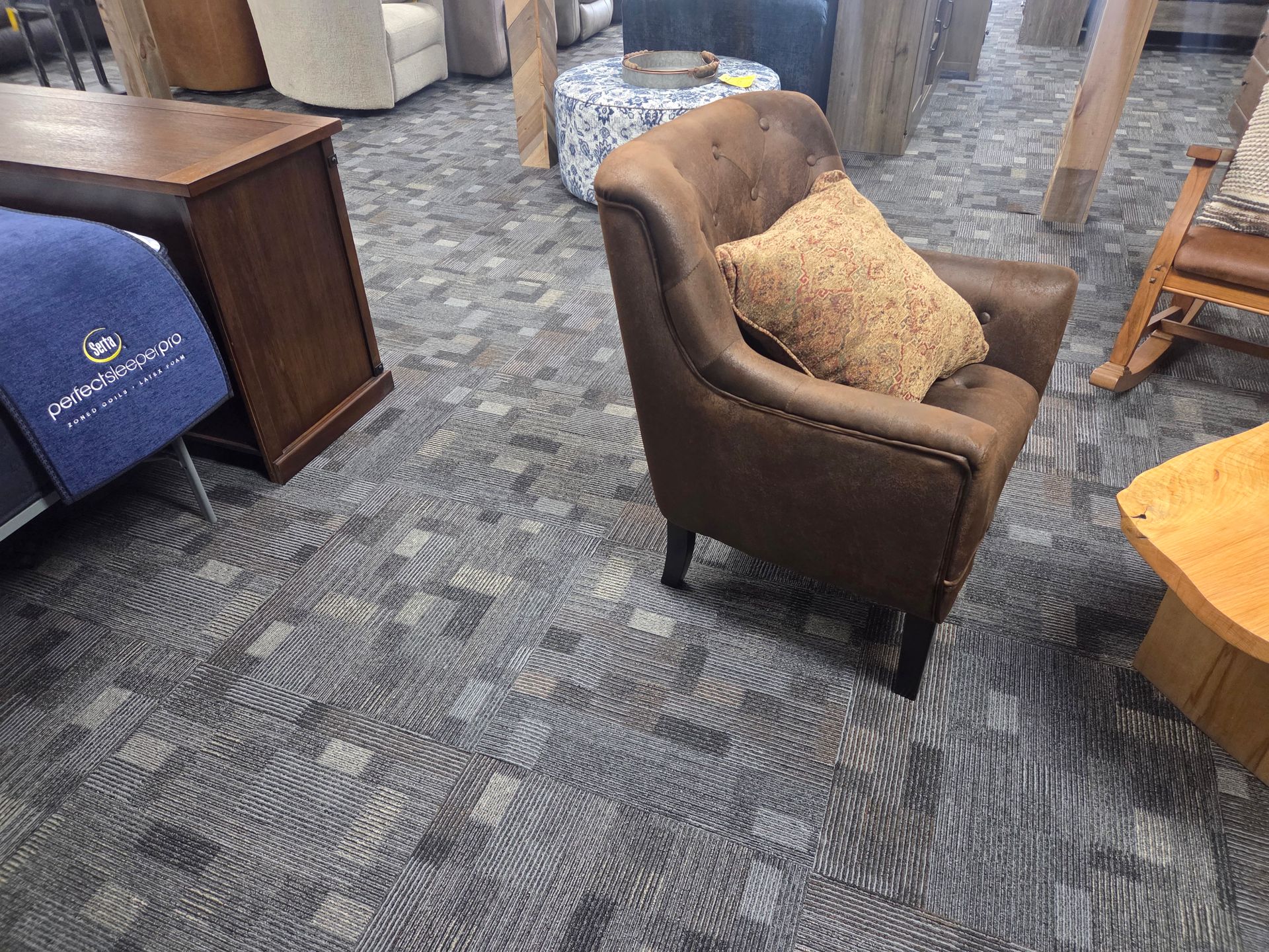 Brown armchair with a throw pillow on patterned carpet in a furniture store.