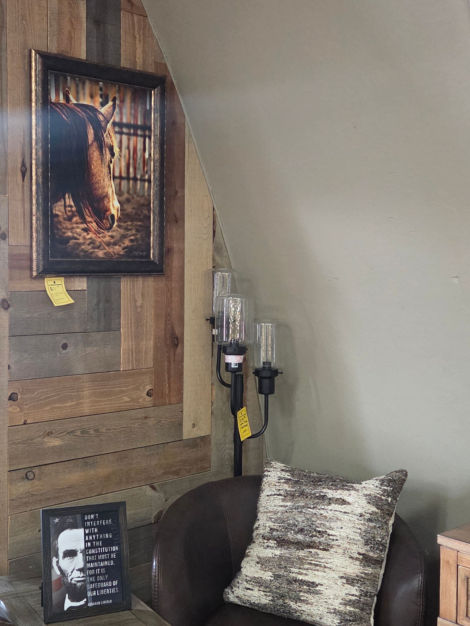 A room corner with a horse picture, a floor lamp, and a brown leather chair with a decorative pillow.