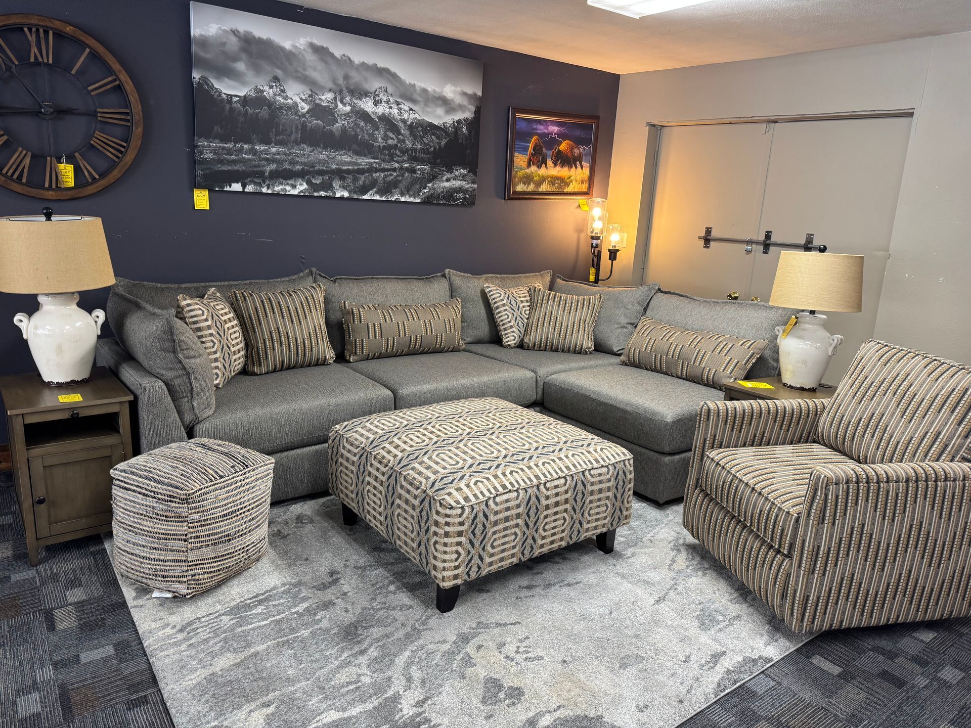 Living room furniture set with gray sectional, ottoman, chair, lamps, and art.