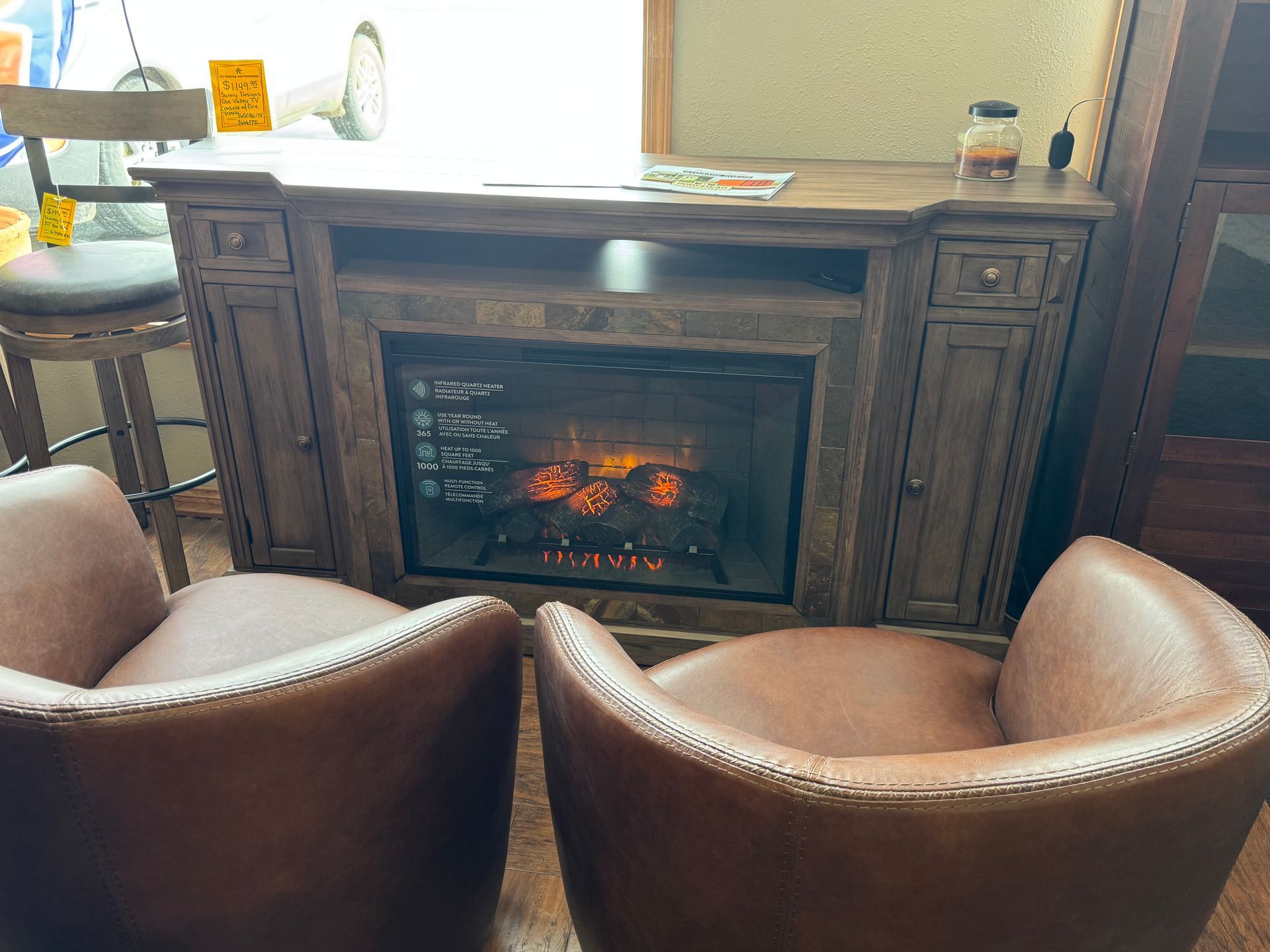 Two leather chairs face a dark wood fireplace entertainment center with a lit flame display.